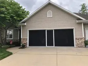 Two-car garage with beige siding, stone accents, and a wide concrete driveway