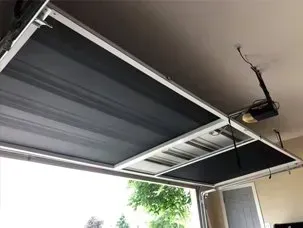 Open garage door with visible opener mechanism and ceiling track, daylight and driveway outside