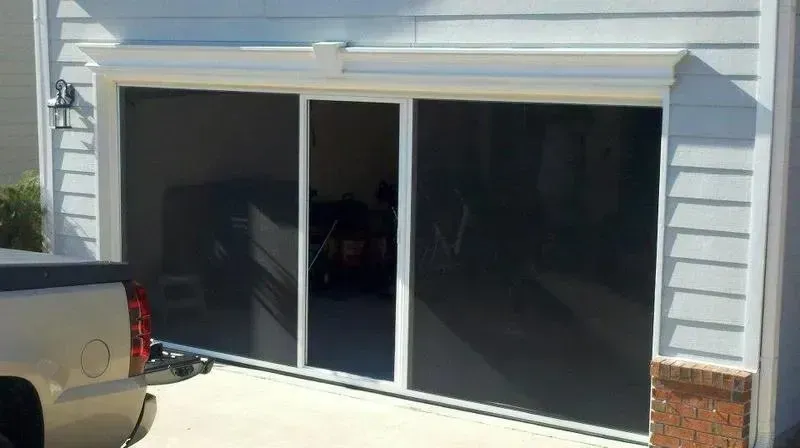 Open garage with dark sliding glass doors beside a white pickup truck in a driveway