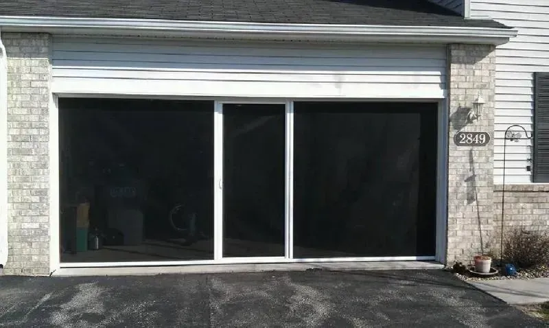 White garage with dark sliding glass doors in a stone house exterior