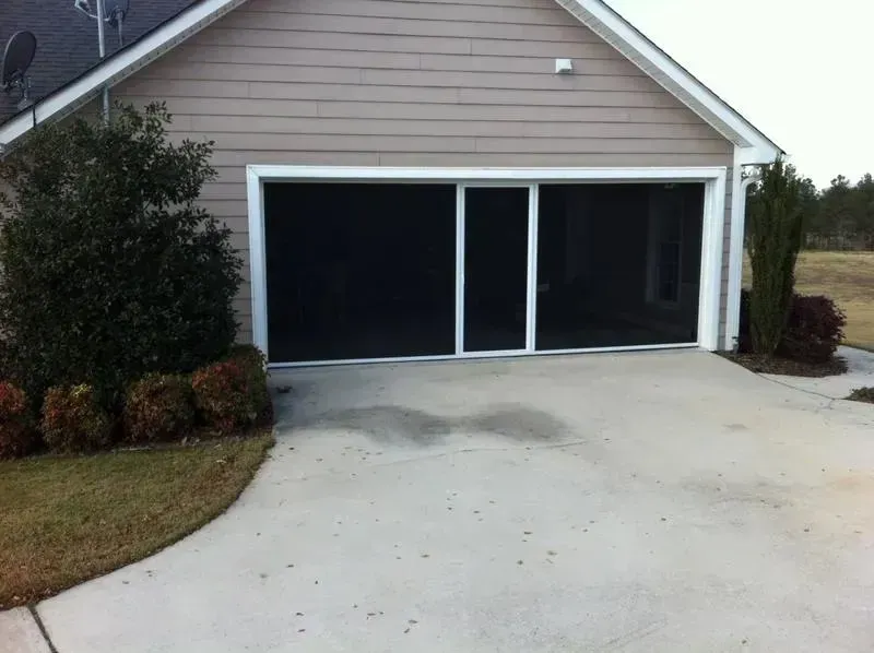 Two-car garage with dark doors and a light concrete driveway in front of a beige house