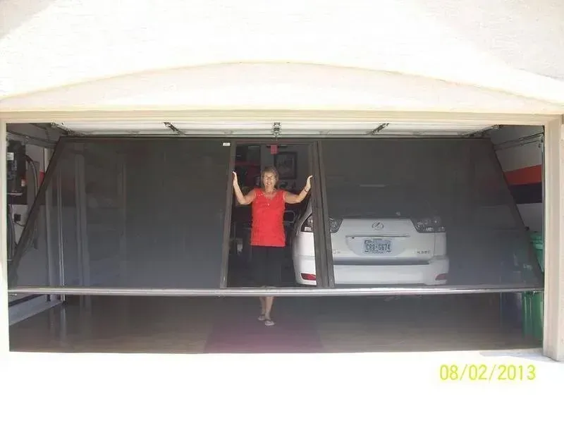 Person in red shirt opening a garage door, with a parked car inside.