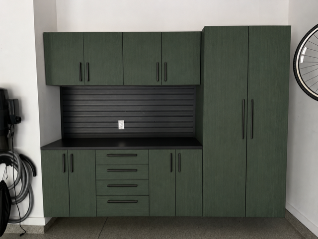 Green garage cabinets with black countertops and a slatted black backsplash against a white wall.