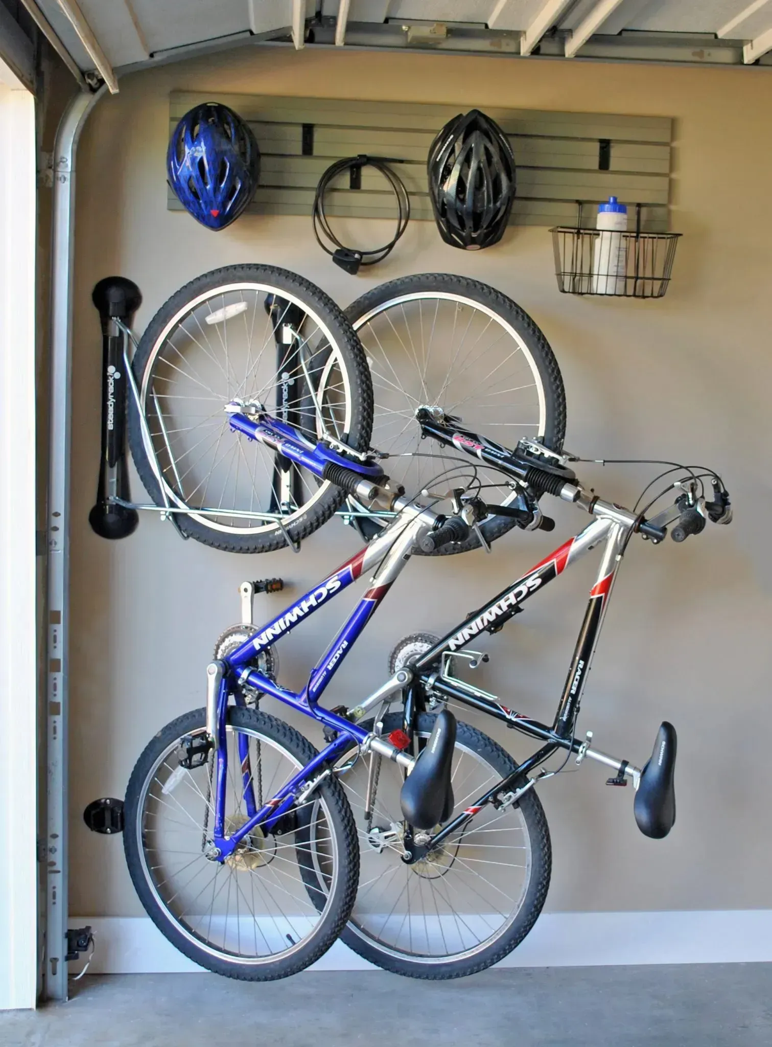 Two bicycles hanging on a wall rack in a garage, with helmets and gear stored above.