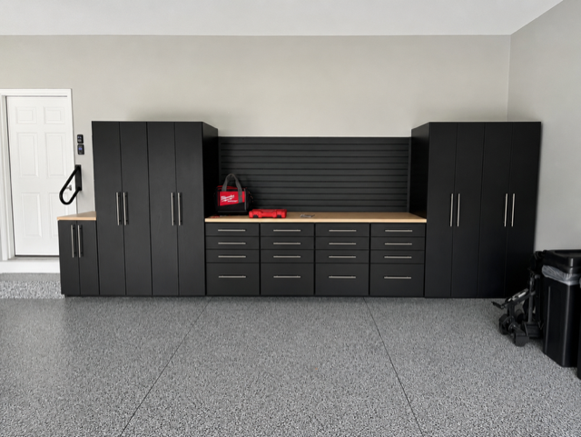 Black garage cabinets and workbench with drawers against a white wall in a carpeted room