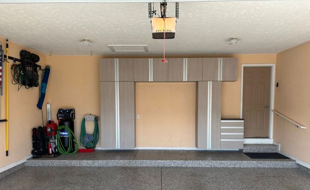 Garage interior with beige walls, gray cabinet storage, and tools along the left side