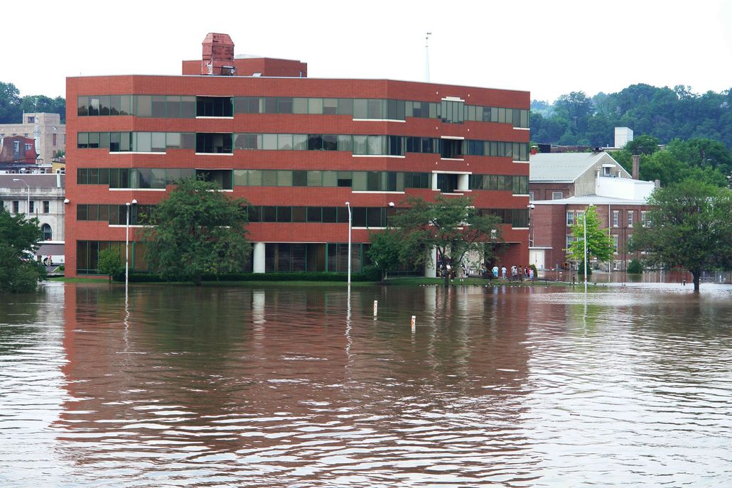 Red brick apartment building partially submerged in floodwater by a riverbank