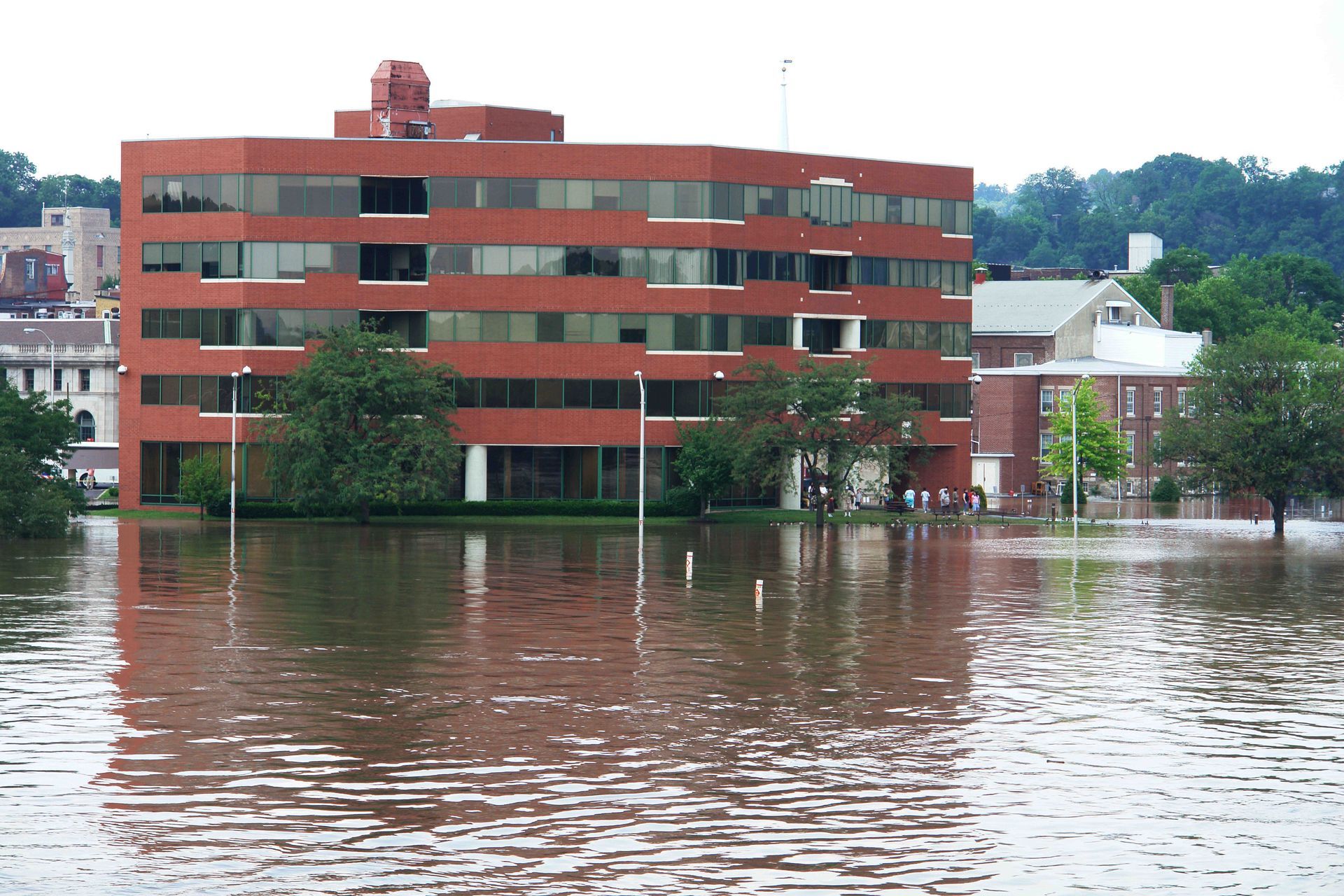 Red brick apartment building partially submerged in floodwater by a riverbank