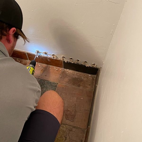 Person using a drill to repair the base of a wall in a tiled corner of a room