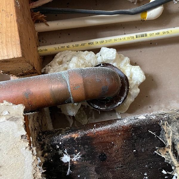 Copper pipe passing through a wall opening sealed with white foam, beside wood framing and wiring.