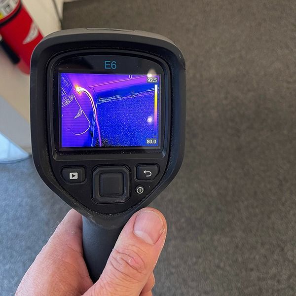 Handheld thermal camera showing a purple-blue heat map on its screen