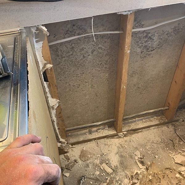 Partially demolished wall exposing studs, insulation, and debris beside a kitchen sink.