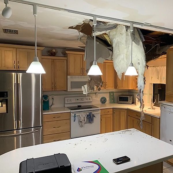 Damaged kitchen with a collapsed ceiling above a white island and hanging drywall over stainless steel appliances