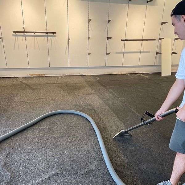 Person smoothing wet concrete floor in a garage-like room with a hose and squeegee.