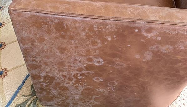 Brown leather ottoman with white water stains and wear on a patterned rug