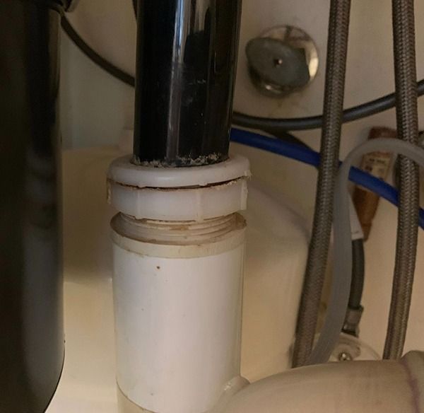 Under-sink plumbing with a white PVC pipe and black drain pipe连接 into a fitting.