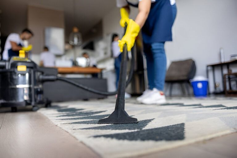 Person vacuuming a rug in a living room, with a yellow glove and a black vacuum cleaner