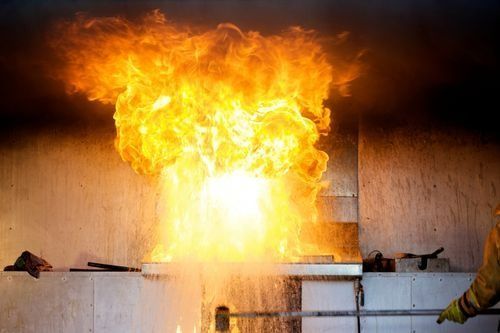Large orange fireball erupts from a wall opening in an indoor industrial setting