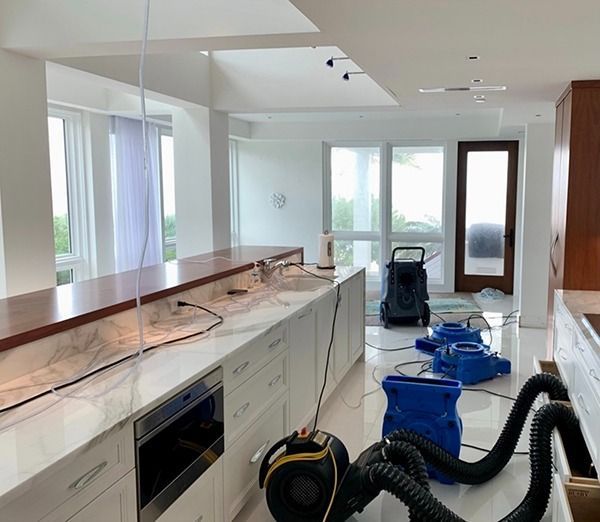 Modern kitchen under renovation with marble island, blue buckets, and cleaning equipment on the floor
