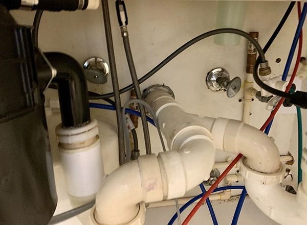 Under-sink plumbing with white PVC pipes, valves, and exposed red and blue water lines