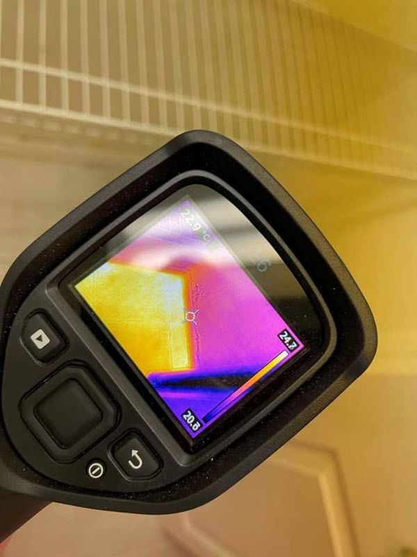Close-up of a small thermal camera screen showing a colorful heat map in a beige indoor setting