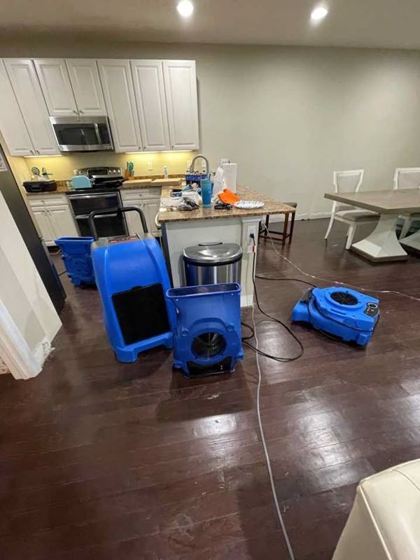 Damaged kitchen floor with blue cleaning equipment and an industrial fan in a home interior