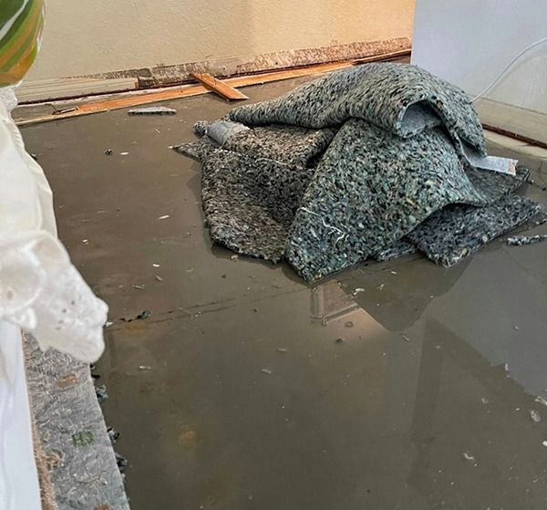Flooded room with a pile of gray carpet or padding on the wet floor.
