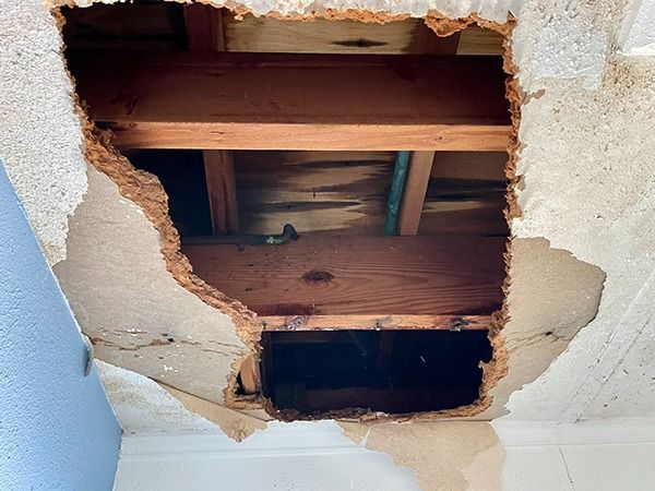 Damaged ceiling with a large hole exposing wooden joists and insulation on a white wall