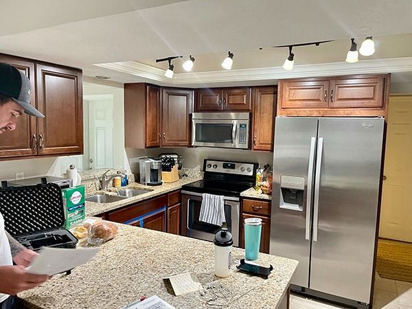 Kitchen with stainless steel appliances and granite island, while a person prepares something at the counter.