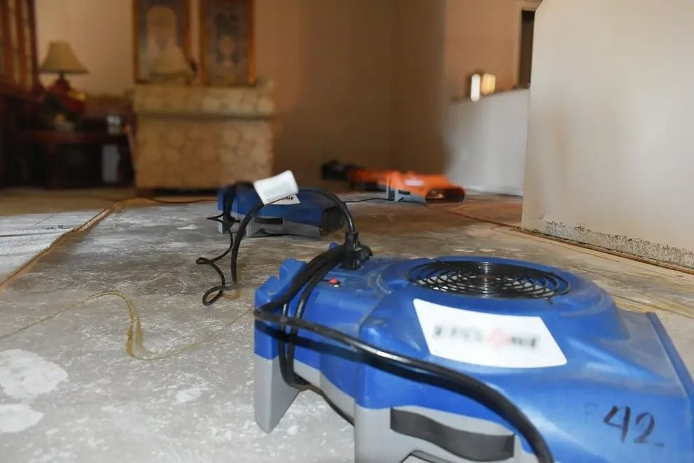 Two blue robots on a concrete floor in a hallway, one in the foreground with wires attached.