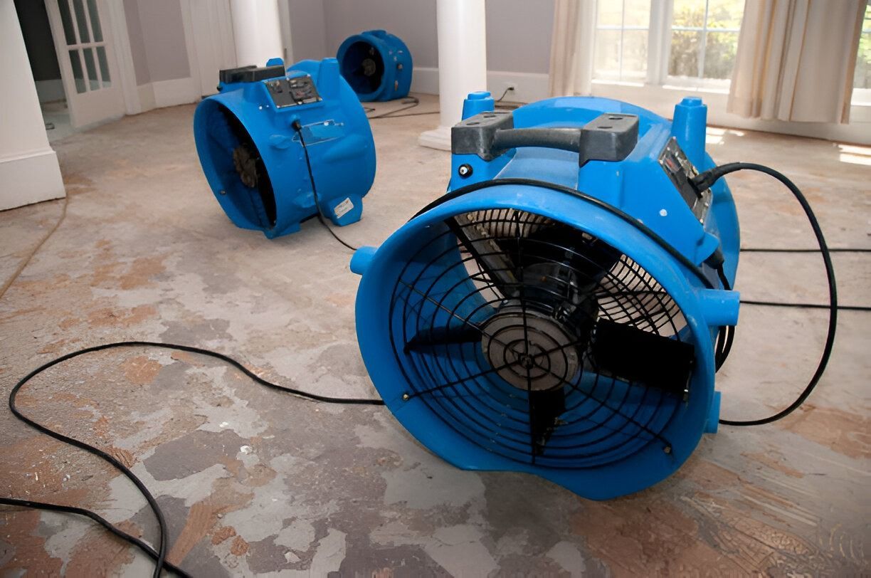 Blue industrial fans in a room with water on the floor, suggesting a drying or cleanup process
