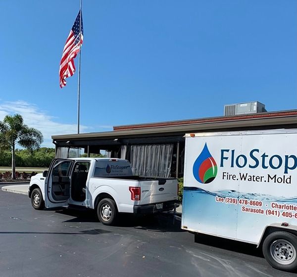 White pickup and FloStop trailer parked by a building under a U.S. flag on a sunny day