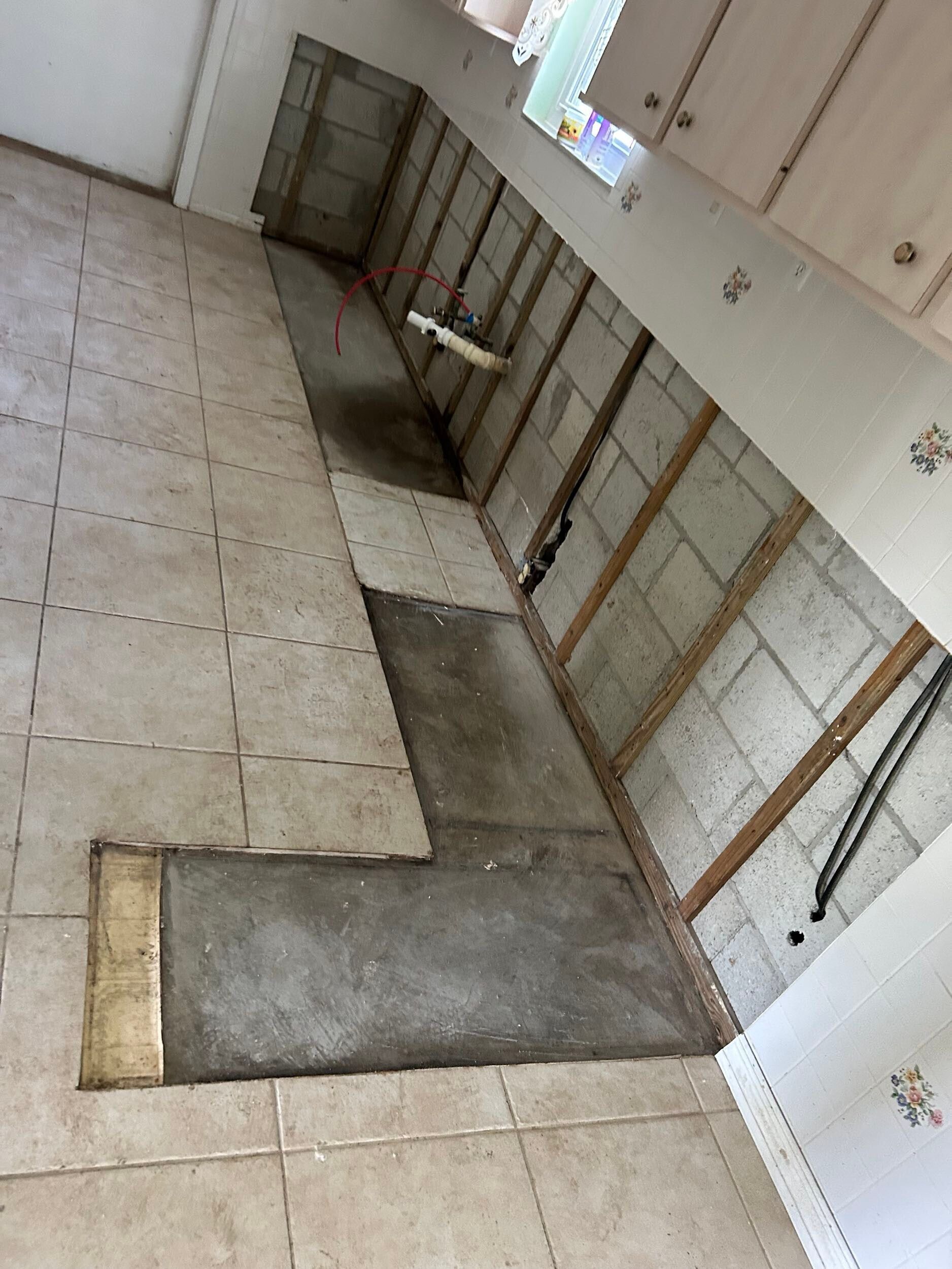 Kitchen under renovation with exposed wall framing, tiled floor, and a concrete work area.