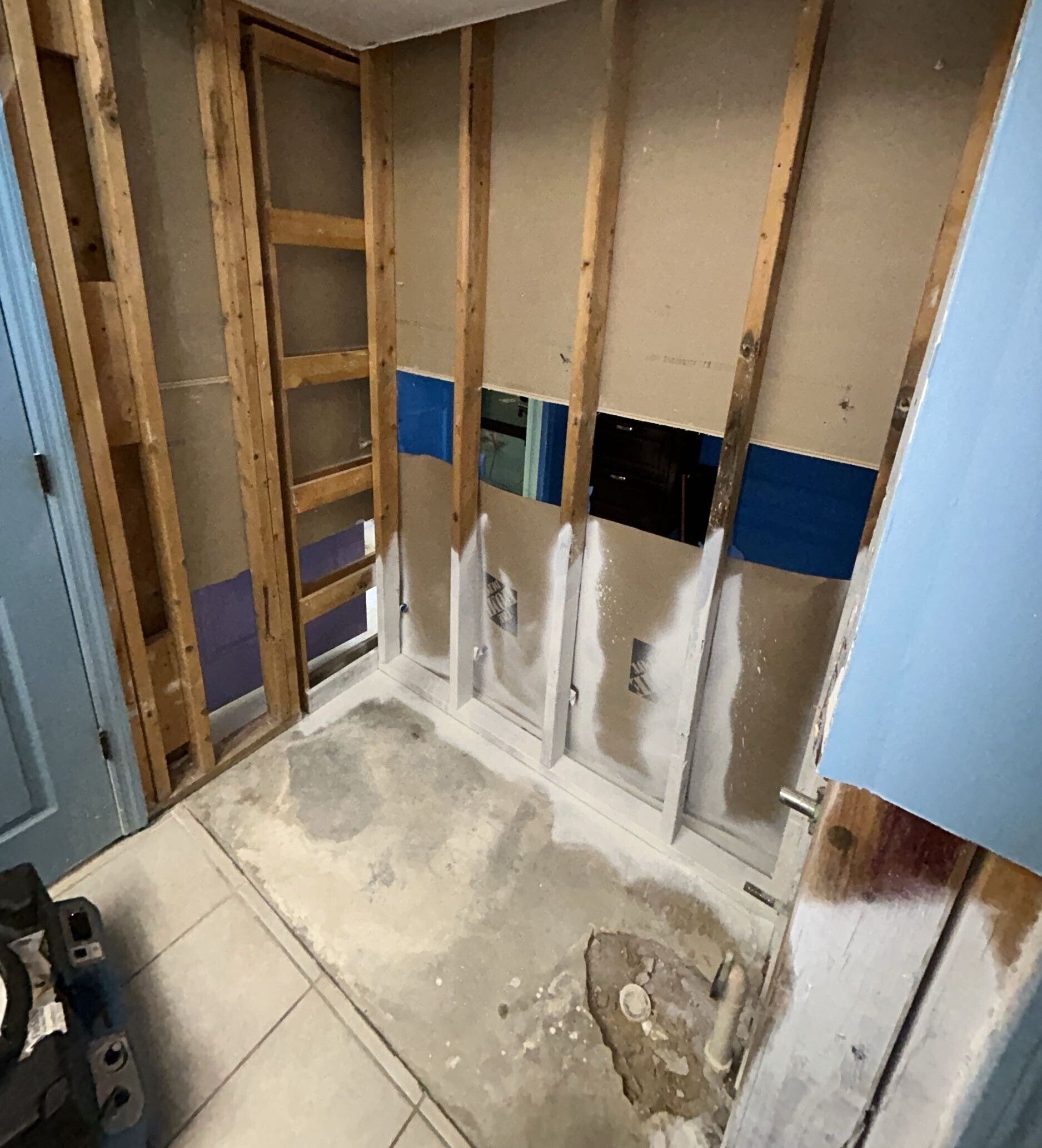 Unfinished bathroom wall with exposed studs, drywall patches, and a rough concrete floor.