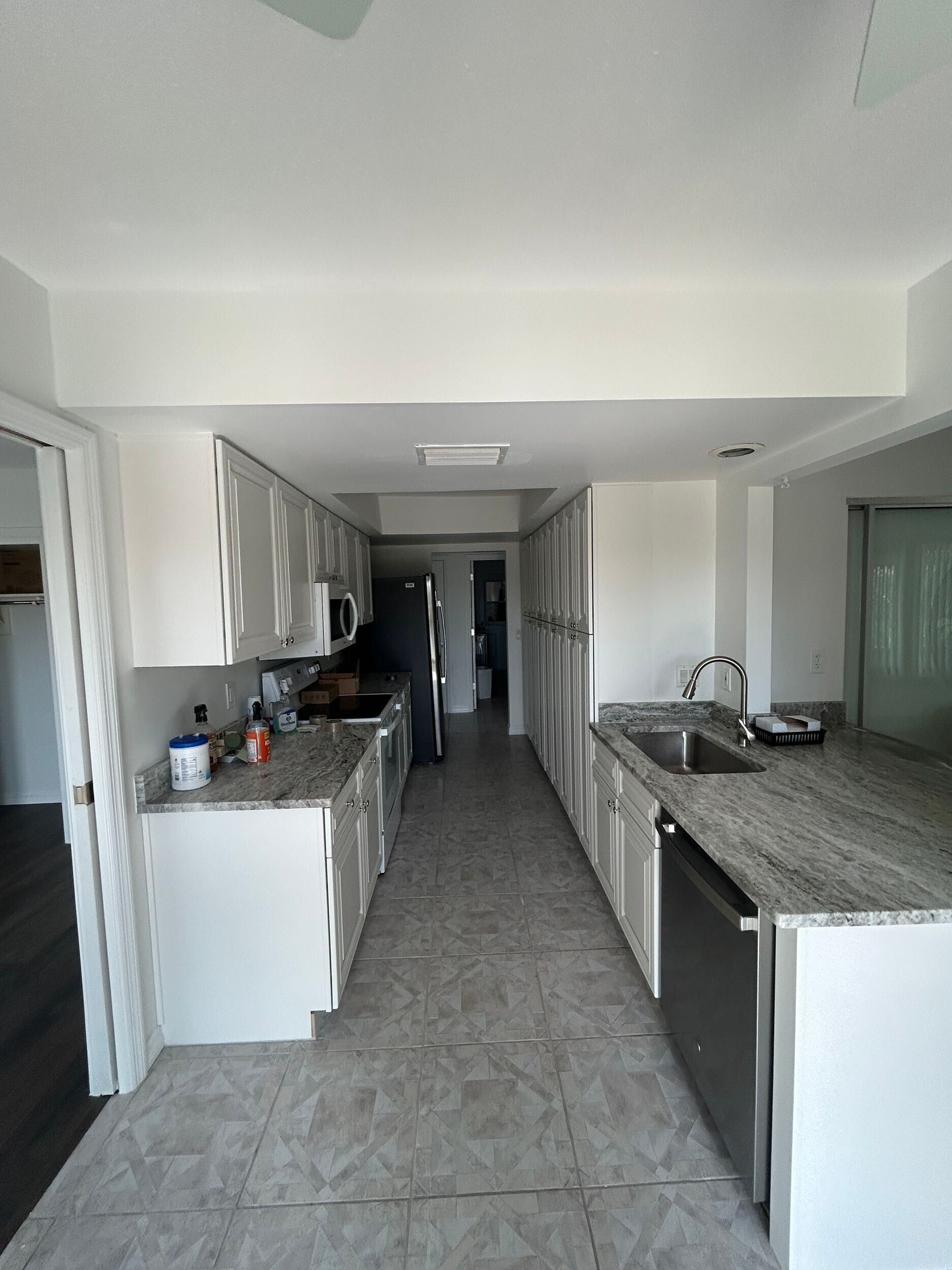 Narrow galley kitchen with white cabinets, gray counters, and tiled floor extending to a back hallway