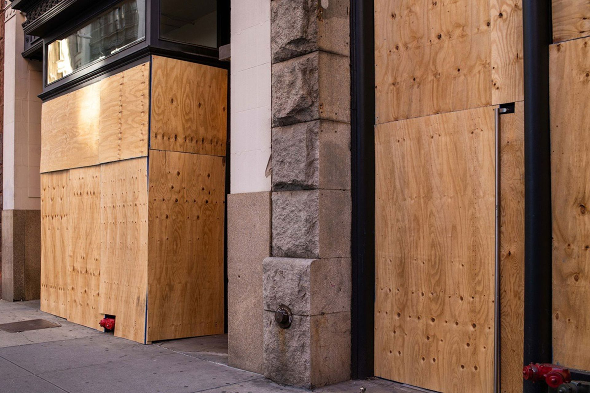 Plywood boards covering storefronts on a stone building along a sidewalk