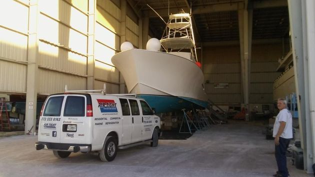 White van and a large boat inside a warehouse, with two people nearby.