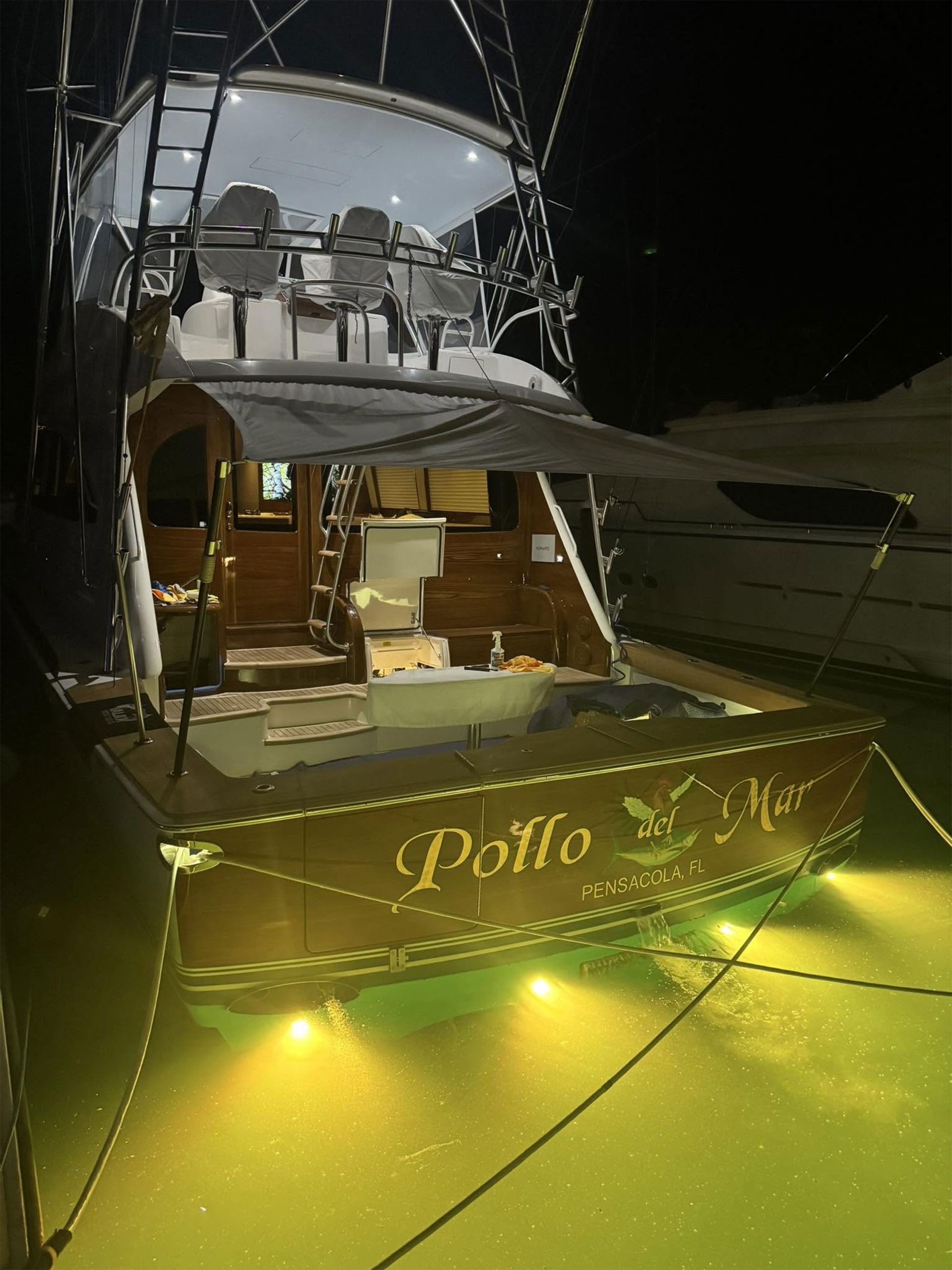 Lit-up docked yacht with open rear deck at night, viewed from the stern.