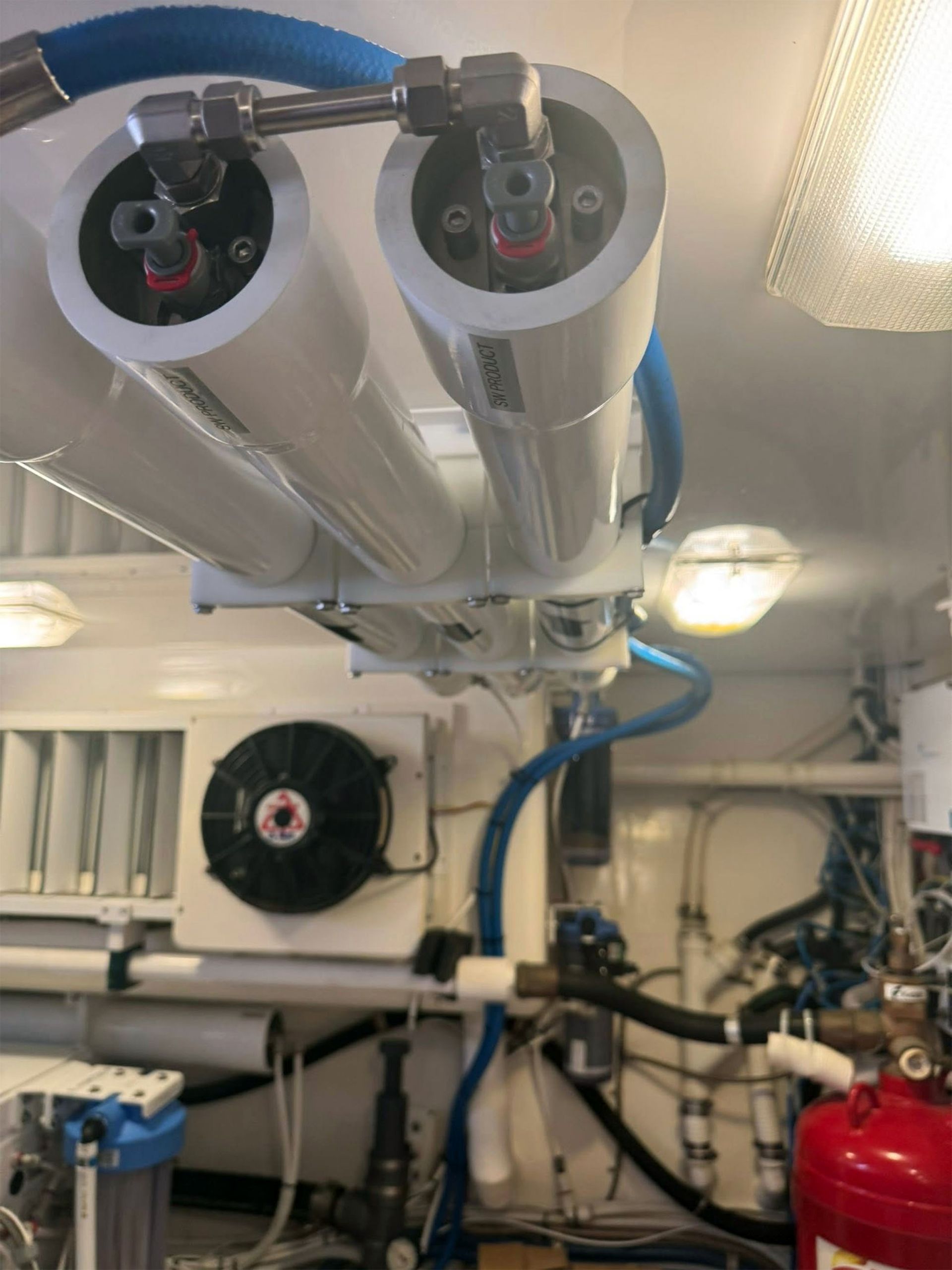 Marine engine room with silver pipes, blue hoses, and a red fire extinguisher mounted on the wall