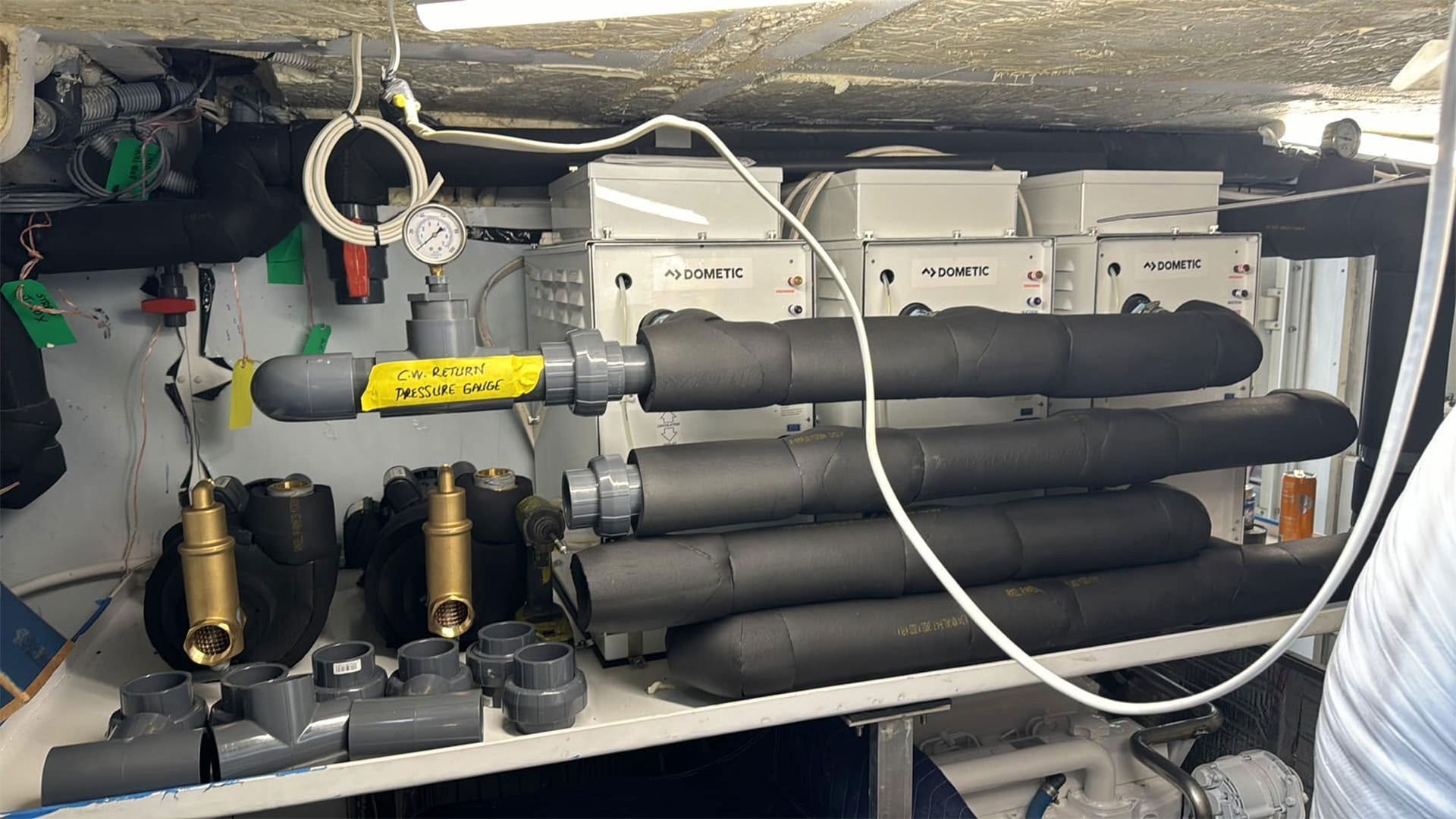 Compact mechanical storage area with stacked gray pipes, valves, and control boxes under a low ceiling
