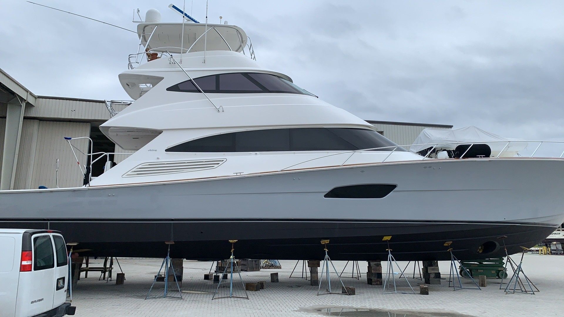 Large white-and-black luxury yacht on stands in a boatyard under a cloudy sky