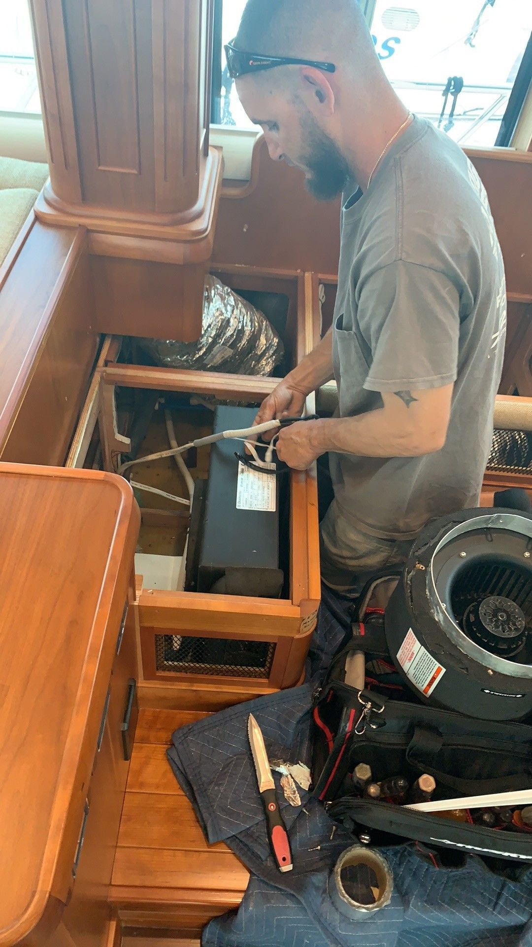 Man in gray shirt repairs a wooden organ beside a wheelchair in a small room