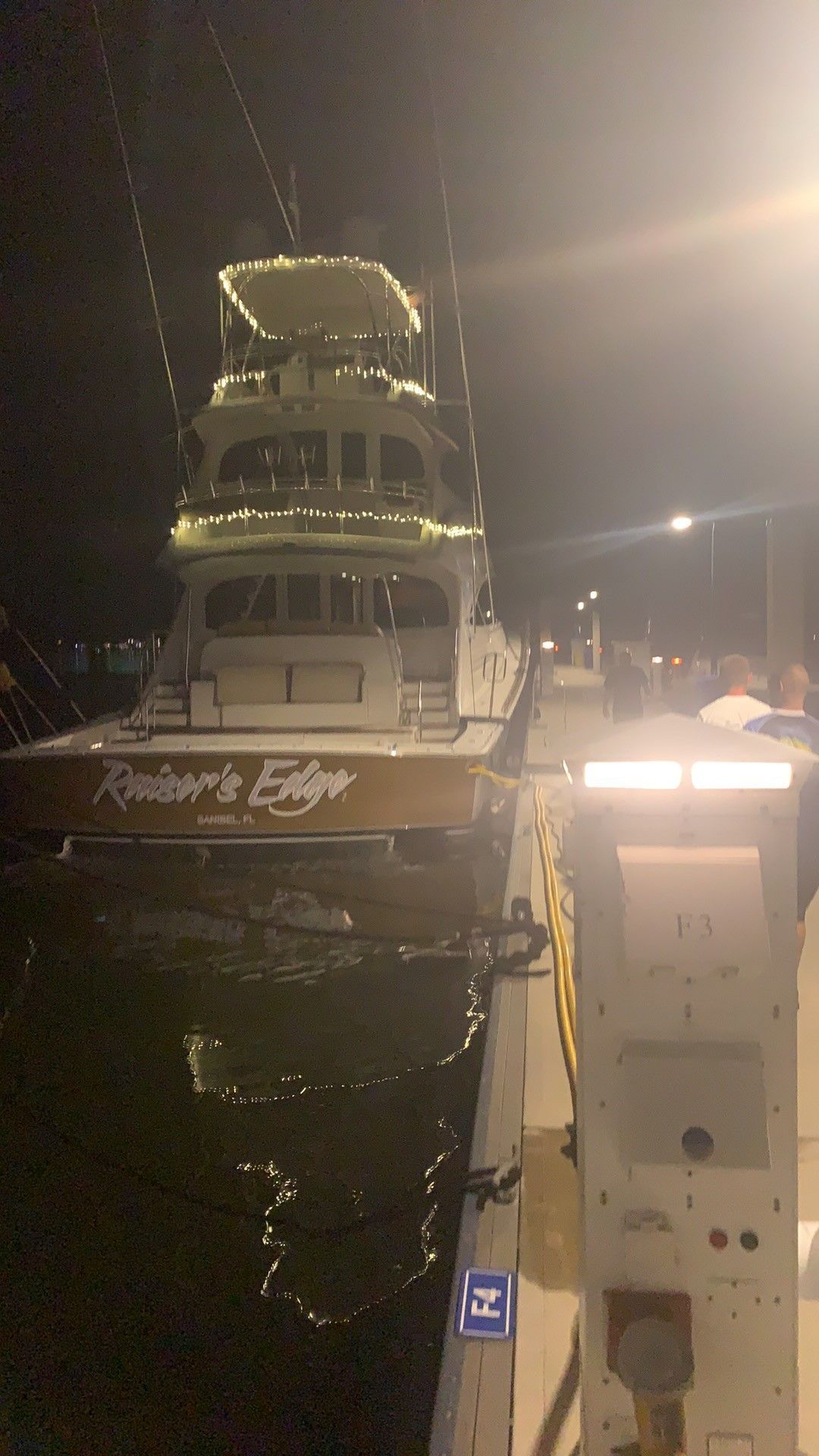 Docked white yacht at night with bright lights reflecting on dark water