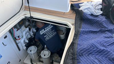Person working in a boat’s engine compartment beside a blue quilted cover