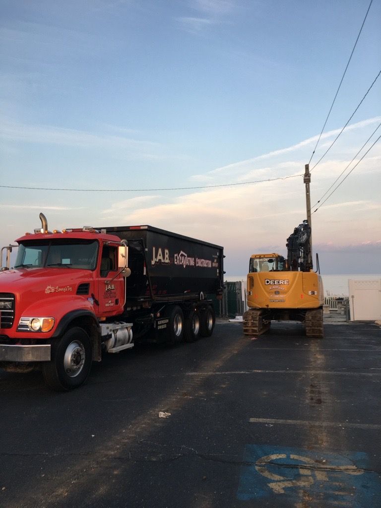 red dump truck next to yellow excavator, on a paved area with a blue sky background