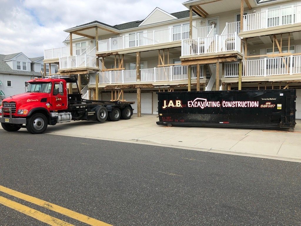 red truck next to a black dumpster in front of a white building with wooden supports