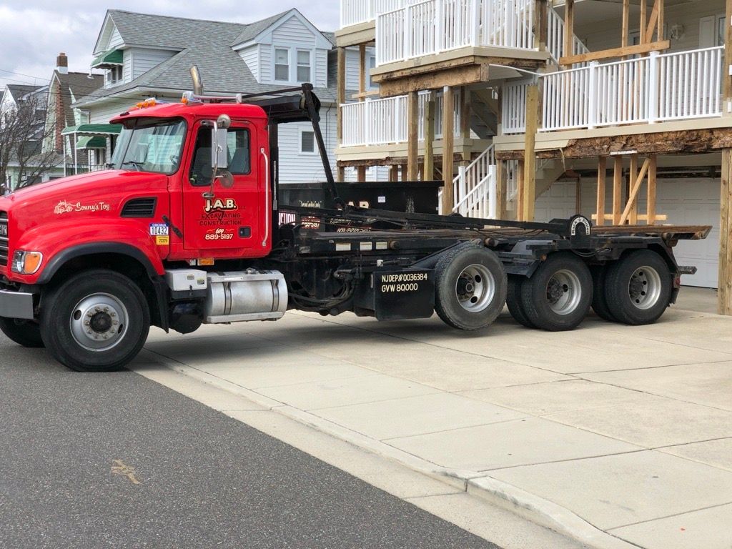 red roll-off truck parked on a street near a building with a wooden balcony
