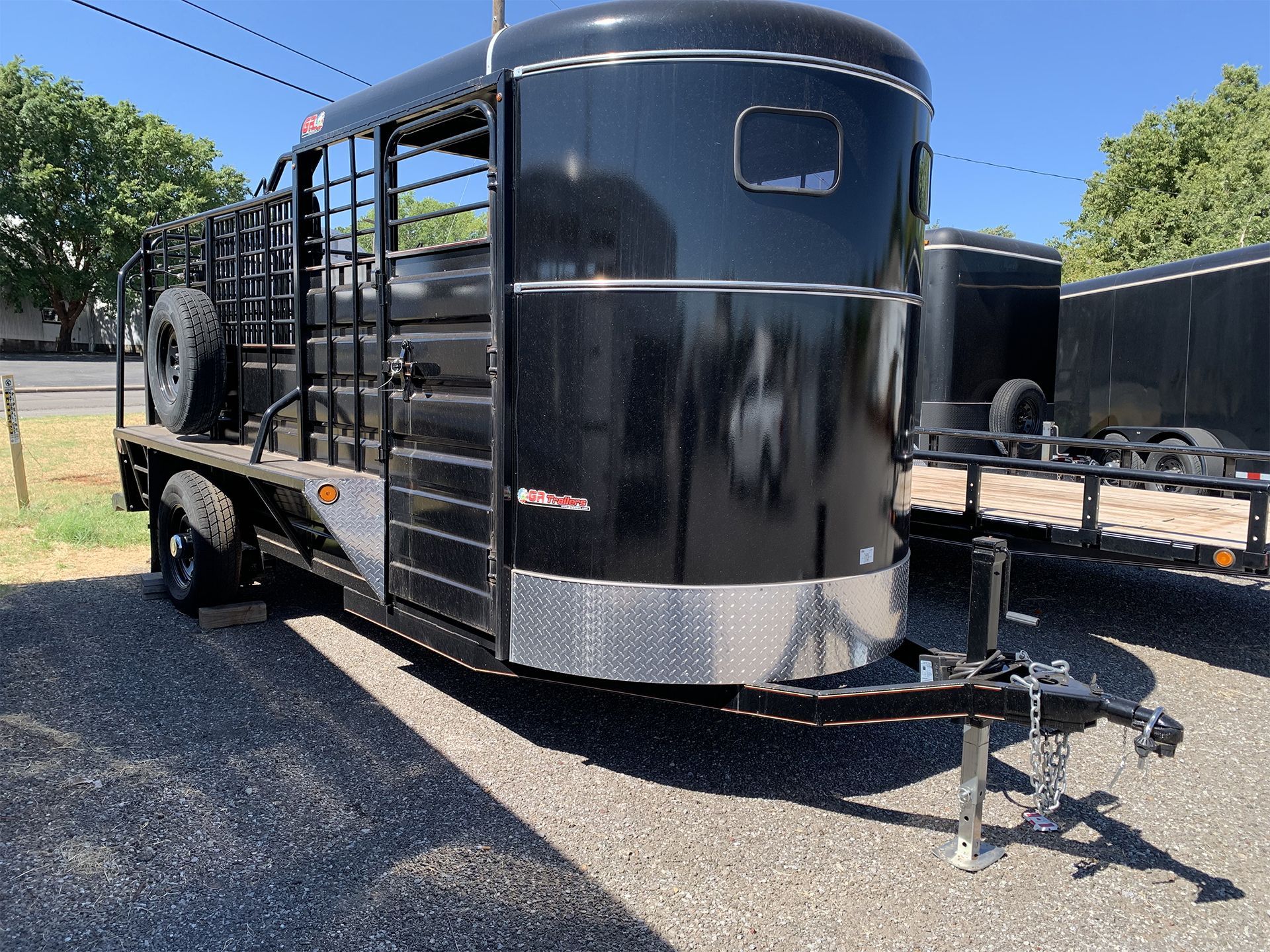 A black horse trailer is parked on the side of the road.