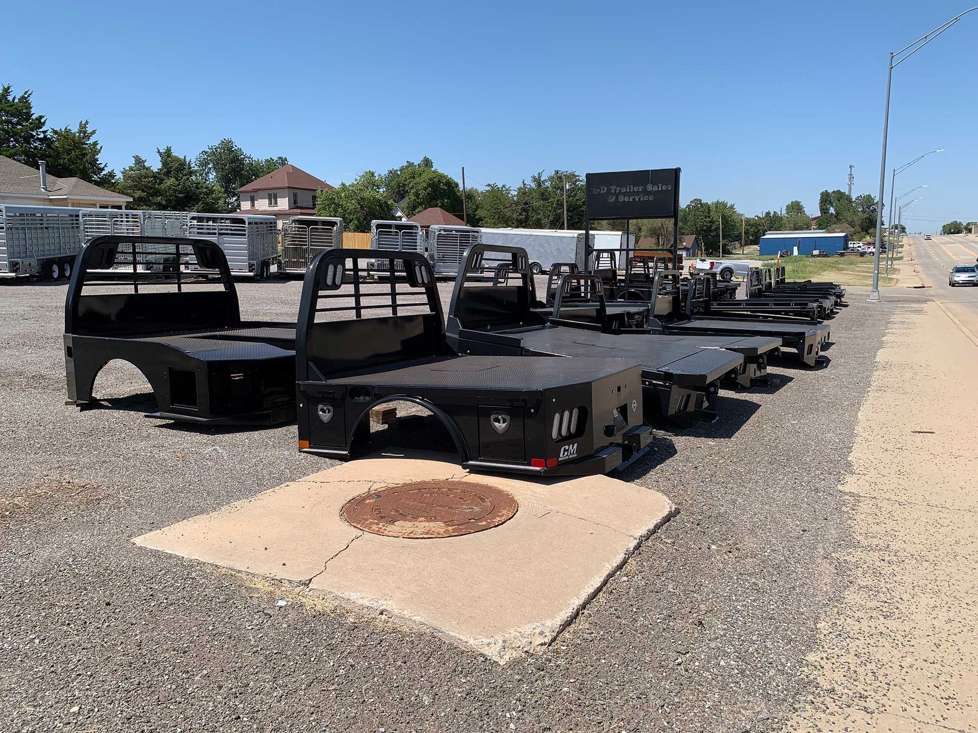 A row of truck beds are lined up in a gravel lot.
