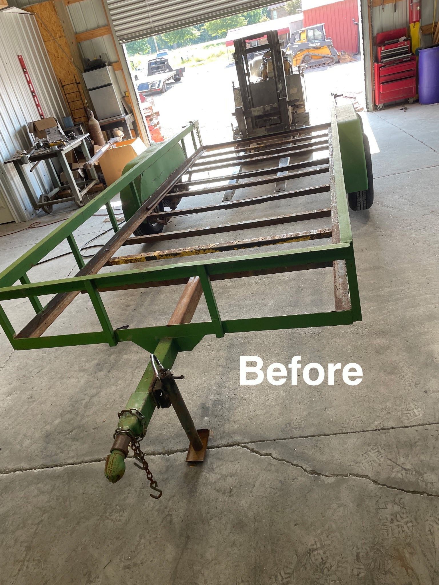 Green trailer frame inside a garage with a tractor in the background. The image is labeled